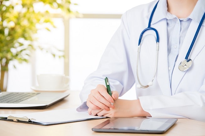 médica escrevendo em pronturário de paciente com hiperaldosteronismo primário, com tablet para consulta ao lado
