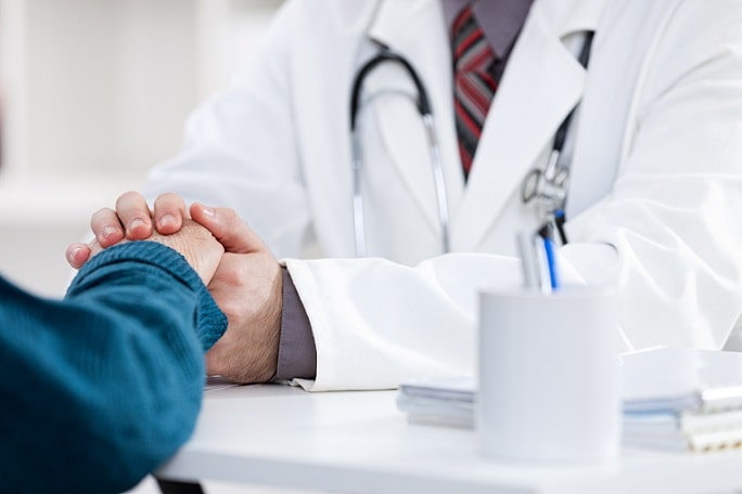 médico segurando a mão de paciente seguindo os atributos da atenção primária, como orientação comunitária e foco na família